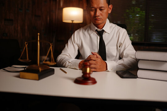 Serious Lawyer Sitting with Hands Clasped at Desk with Scales of Justice and Gavel