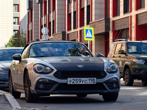 Silver Abarth 124 Spider luxury compact roadster model car parked outdoors. Premium Italian rear-wheel drive RWD sports automobile with matte black hood bonnet and stylish convertible design profile. 