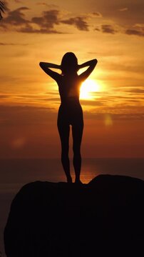 Silhouette of Young Woman Standing on Rock at Golden Sunset
