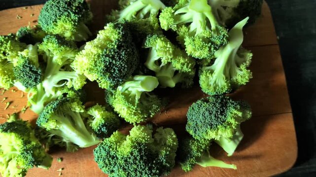 High angle view of fresh broccoli pieces scattered on wooden board with smooth camera motion revealing green raw vegetables for culinary content creation.