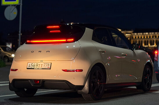 Stylish modern Ora 03 Good Cat electric hatchback car parked on a city street at night. Premium Chinese EV automobile with a glowing red LED taillight strip, neo-retro design, and two-tone body color.