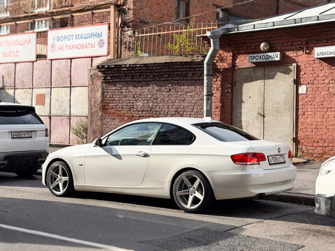 White BMW 3 Series E92 luxury sport coupe car parked outdoors on an asphalt road. Premium German RWD or xDrive sports automobile engineered on an E90 platform chassis with an elegant body silhouette.