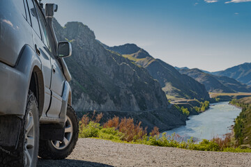 Low angle side view of an off-road 4x4 suv car parked on a cliff ledge overlooking a scenic mountain river canyon, overlanding concept © ANDREY