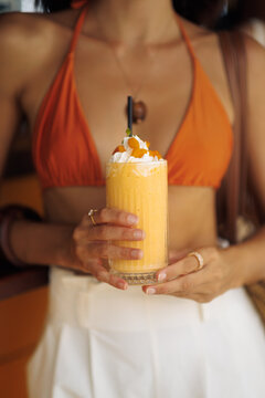 Mango Smoothie with Cream Topping Held by Woman in Orange Bikini Close