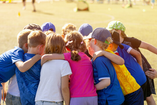 Group of Diverse Children Standing in Team Huddle with Arms Around Shoulders - Youth Sports Team Unity, Support, and Friendship Concept