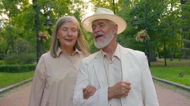 Happy Caucasian elderly couple walking holding hands love walk in city park smiling talking retired senior family man and woman enjoying romantic date relationship active retirement travelling outdoor