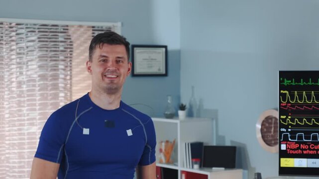 An adult male athlete wearing a blue athletic shirt with electrodes attached to his torso, smiling during a medical diagnostic test in a clinical laboratory setting.