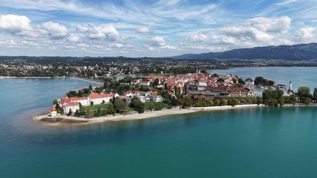 Aerial panoramic view of Lindau Island on Lake Constance in Bavaria, Germany, with the historic old town, marina, waterfront and green Alpine foothills under a dramatic summer sky.