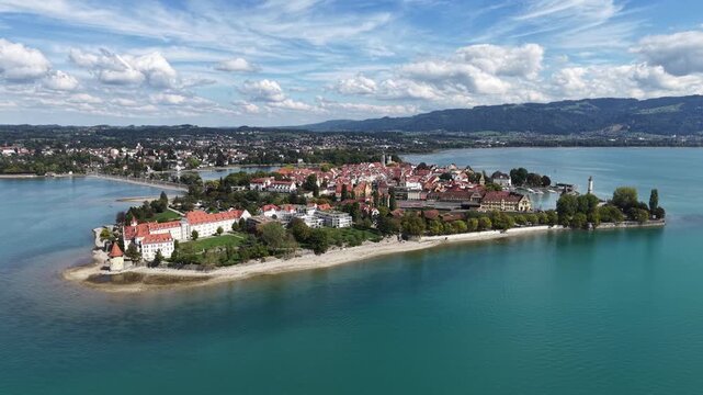 Aerial panoramic view of Lindau Island on Lake Constance in Bavaria, Germany, with the historic old town, marina, waterfront and green Alpine foothills under a dramatic summer sky.