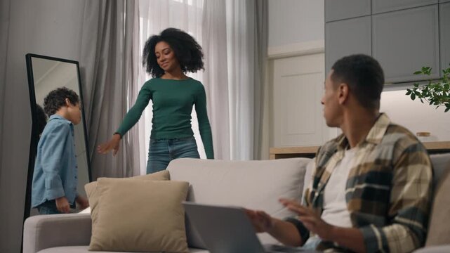 Angry African American father freelancer working laptop yelling noisy mother son dancing little child boy mom having fun move leaving family quarrel busy annoyed dad parents problem indoors home room