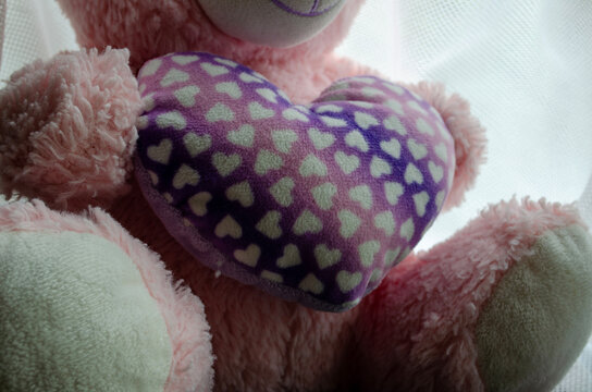 Soft teddy bear holding a heart-shaped cushion with small hearts