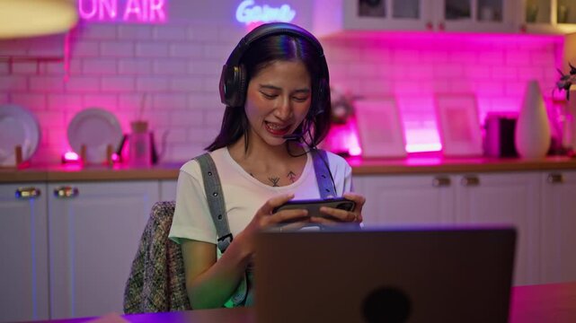 Asian young e-sport woman gamer play online mobile game on smartphone.Attractive girl vlogger influencer content creator gamer enjoy and fun live streaming broadcast games in POV screen and neon room.