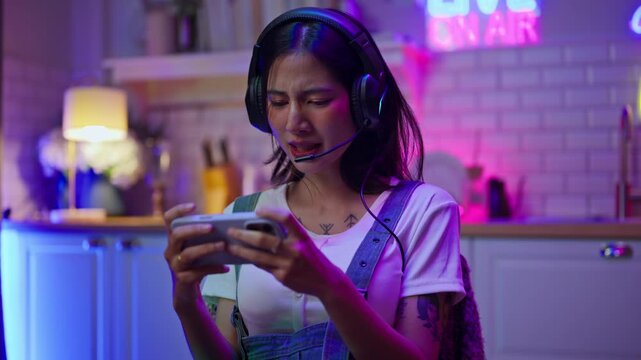 Asian young e-sport woman gamer play online mobile game on smartphone.Attractive girl vlogger influencer content creator gamer enjoy and fun live streaming broadcast games in POV screen and neon room.