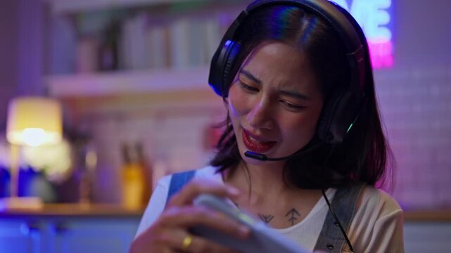 Asian young e-sport woman gamer play online mobile game on smartphone.Attractive girl vlogger influencer content creator gamer enjoy and fun live streaming broadcast games in POV screen and neon room.