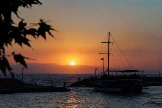 Scenic view of a two-masted pleasure boat sailing in the Mediterranean sea against a vibrant orange sunset sky in Side.