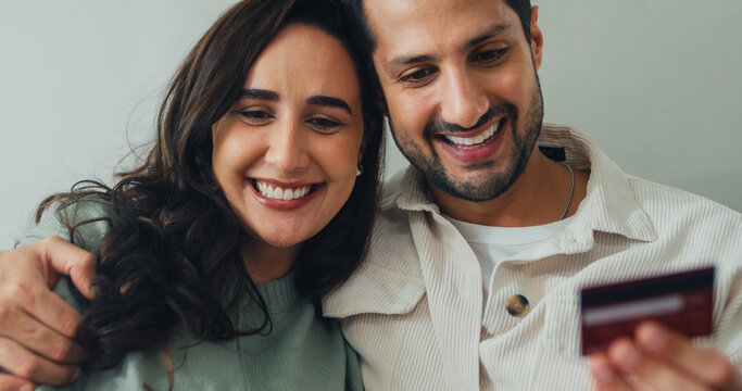 Young Latin couple male, female customers paying by credit card online and laptop shopping online furniture decorate on sofa in living room at home. Young married moving home shopper online concept.