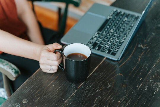 Person working on a laptop while holding a cup of coffee on a dark wooden table