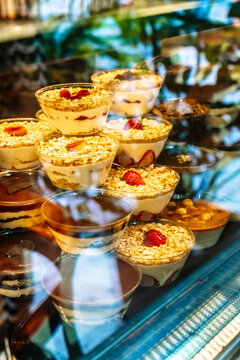 Assorted layered desserts in clear plastic cups displayed in a refrigerated bakery case