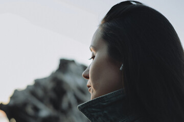 Pensive woman standing by the sea in soft natural light, viewed in close profile with long dark hair, creating a quiet atmospheric portrait about solitude, reflection, emotional travel and inner calm. © vita