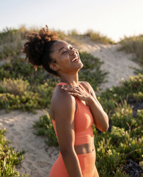 Woman laughs freely with her hand on her shoulder amid coastal dune grass