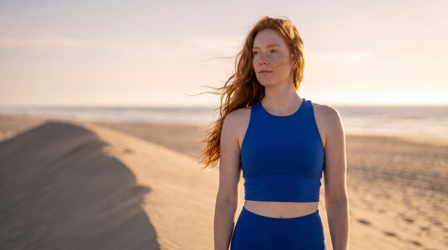 Windswept redhead stands tall on a beach dune gazing toward the horizon