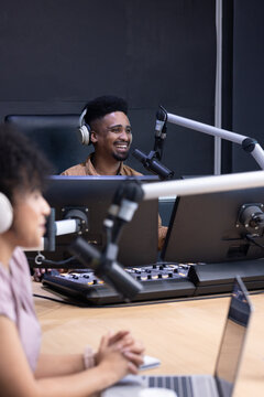 African American coworkers smiling and speaking into mics while operating mixing console at studio