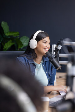 Adult African American female podcaster in denim and white headset speaking into mic in studio