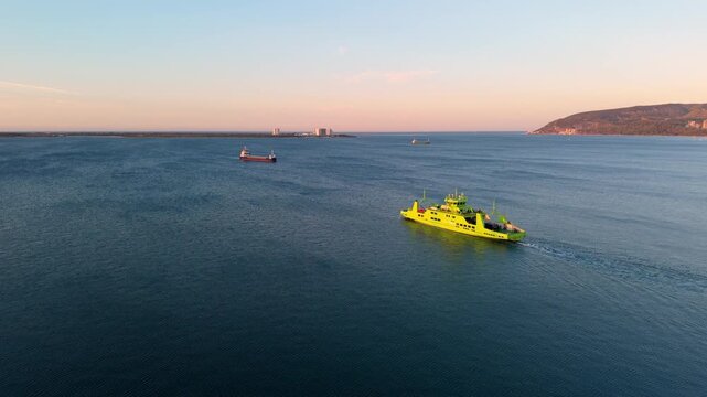 Aerial view of calm sea with yellow rescue boat and cargo ships. Warm sunset light reflects off water surface. Hills and distant shoreline frame peaceful maritime scene. Ideal for travel, safety