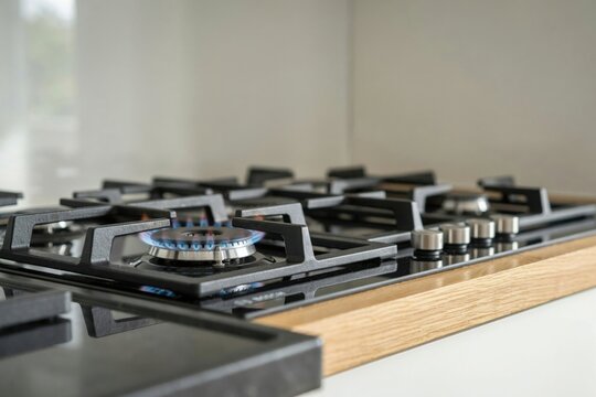 Modern black gas stovetop with a burning blue flame in a contemporary kitchen with wood counter