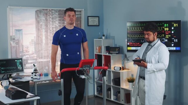 An athlete wearing electrodes walks on a treadmill while a doctor in a lab coat monitors vital signs in a medical laboratory during daytime.
