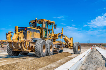 Fototapeta premium Motor grader prepares ground for roads and infrastructure in neighborhood. Construction, land development.