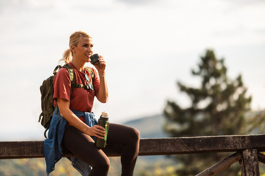 Woman enjoying a drink while resting on a wooden railing during a hike