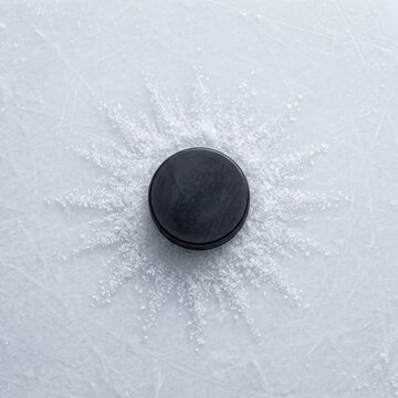 Black hockey puck on ice with snow spray