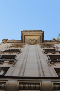 Low angle view from below of classic Haussmann architecture building facade with balconies and ornate details against blue sky in Paris, France. Urban architecture and real estate concept.