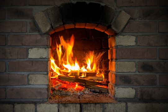 A brightly blazing fire with burning logs inside the brick firebox of a stove.
