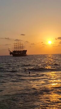 Tall sailing ship moving across the sea at sunset with golden sky reflections