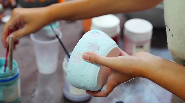 Woman painting floral details on handmade ceramic mug with fine brush. Detailed pottery decoration represents craftsmanship and creative ceramic art
