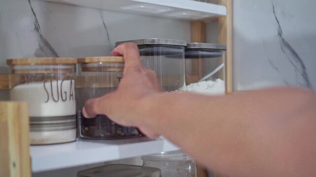 Hand reaching for a tea jar on an organized kitchen pantry shelf. Culinary footage showing cooking ingredients, storage, and home kitchen organization.