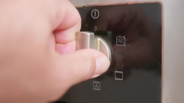 Close-up of a hand operating the different modes dial on an old electric kitchen oven. A mode is selected and the oven operation light activates.