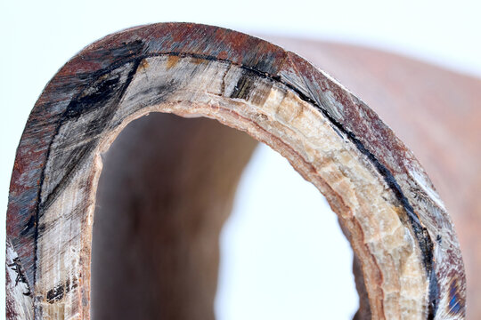 Section of industrial hot water boiler pipe with limescale deposits inside wall, reducing heat transfer efficiency, causing energy loss, corrosion, plumbing blockage, equipment failure
