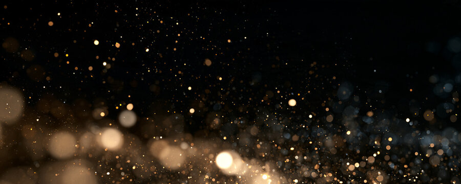 Gold dust particles scatter in a dark space. The tiny specks glow with soft warm light and varying intensity. This image captures a sparkling bokeh effect perfect for festive or background.