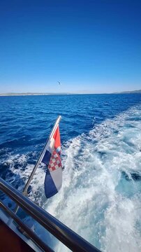Croatian flag fluttering on a boat stern while sailing through blue sea under clear sky
