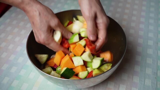 Mixing Fresh Vegetables by Hand. A colorful mixture of pumpkin, zucchini, eggplant and other vegetables is gently combined by hand before cooking.