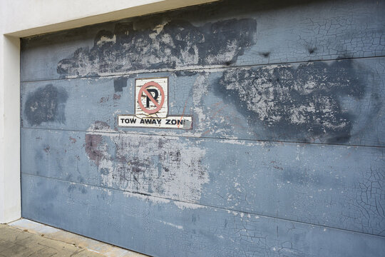 "No Parking: Tow Away Zone" Sign on Weathered and Discolored Garage Door, Which has been Spray Painted to Cover Graffiti