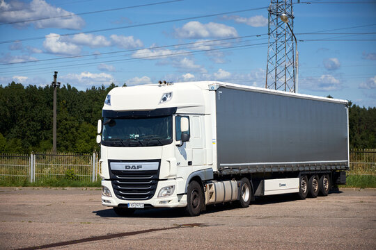 Berlin, Germany - August, 13 2026: White DAF XF semi truck with Krone trailer parked at roadside lot under sunny blue sky with clouds near forest line