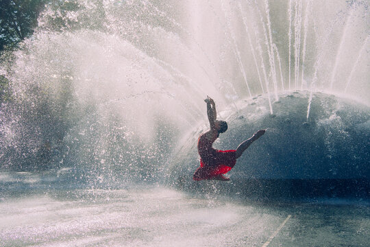 White dancer leaping near water fountain splashes outdoors