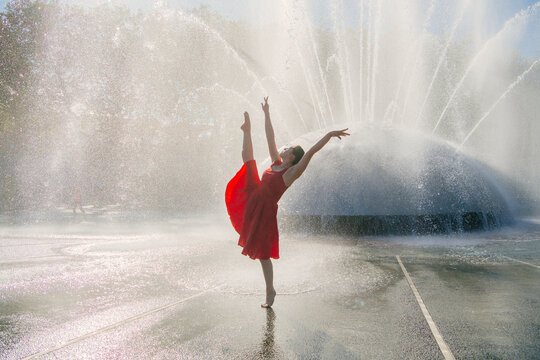 White dancer in red dress striking a graceful pose by outdoor water