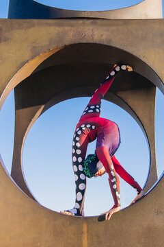 Contortionist in red polka dot costume balancing in circular arch