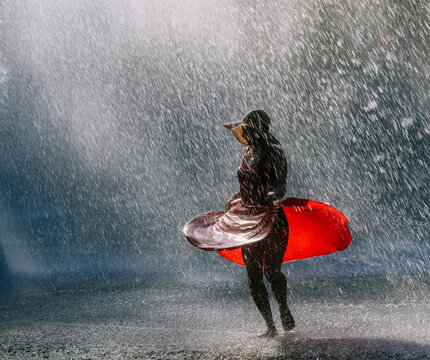 White woman dancing in water spray wearing red dress and sun hat