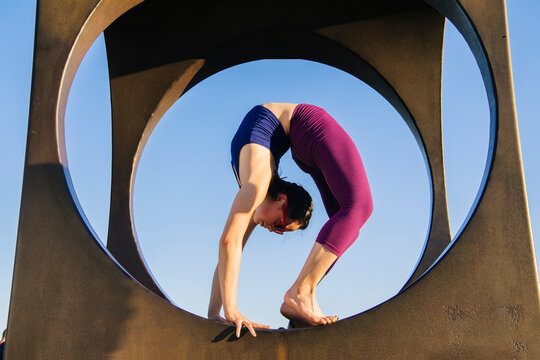 White woman performing backbend yoga pose framed by circular sculpture